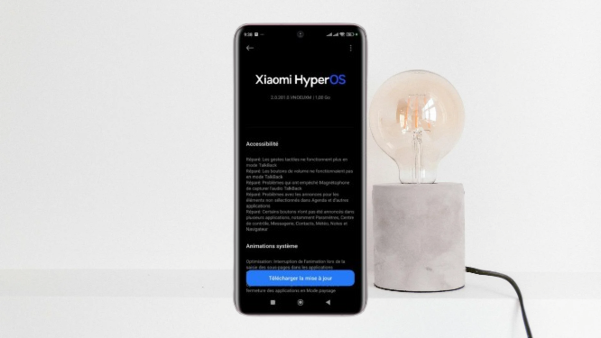 Smartphone showing Xiaomi HyperOS 2.2 update information with French details, next to a modern lamp.