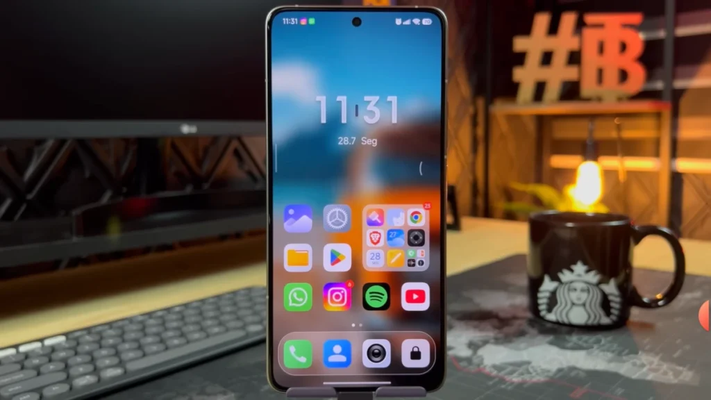 Xiaomi smartphone displaying the home screen with New HyperOS 3 Apps with new icons and widgets, on a desktop setup with a monitor and decorative objects.
