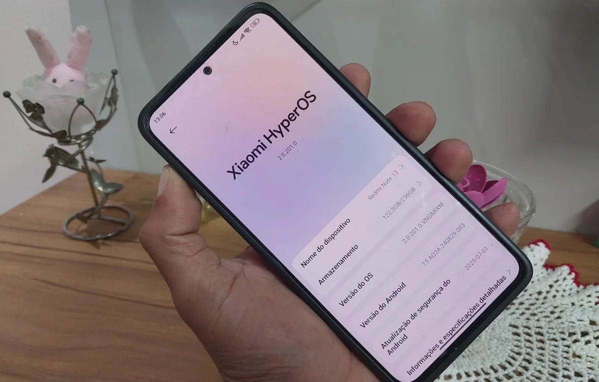Hand holding a Redmi Note 13 4G smartphone with the screen showing HyperOS 2.2 system information.