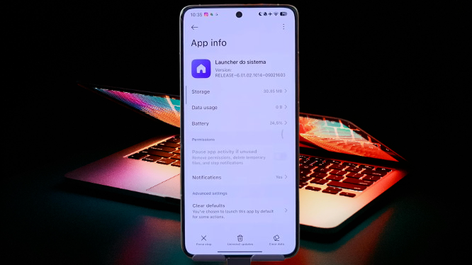 A smartphone displays the "System Launcher" app settings, representing HyperOS Launcher 3, overlaying a notebook with a backlit keyboard.