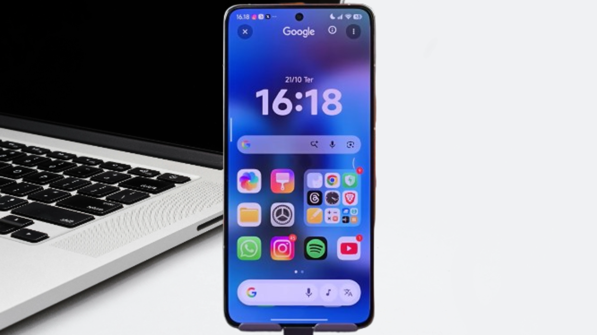 Smartphone displaying the HyperOS Launcher 3 home screen, featuring a vibrant blue wallpaper, prominent time and date widget, and organized app icons, with a laptop in the background.