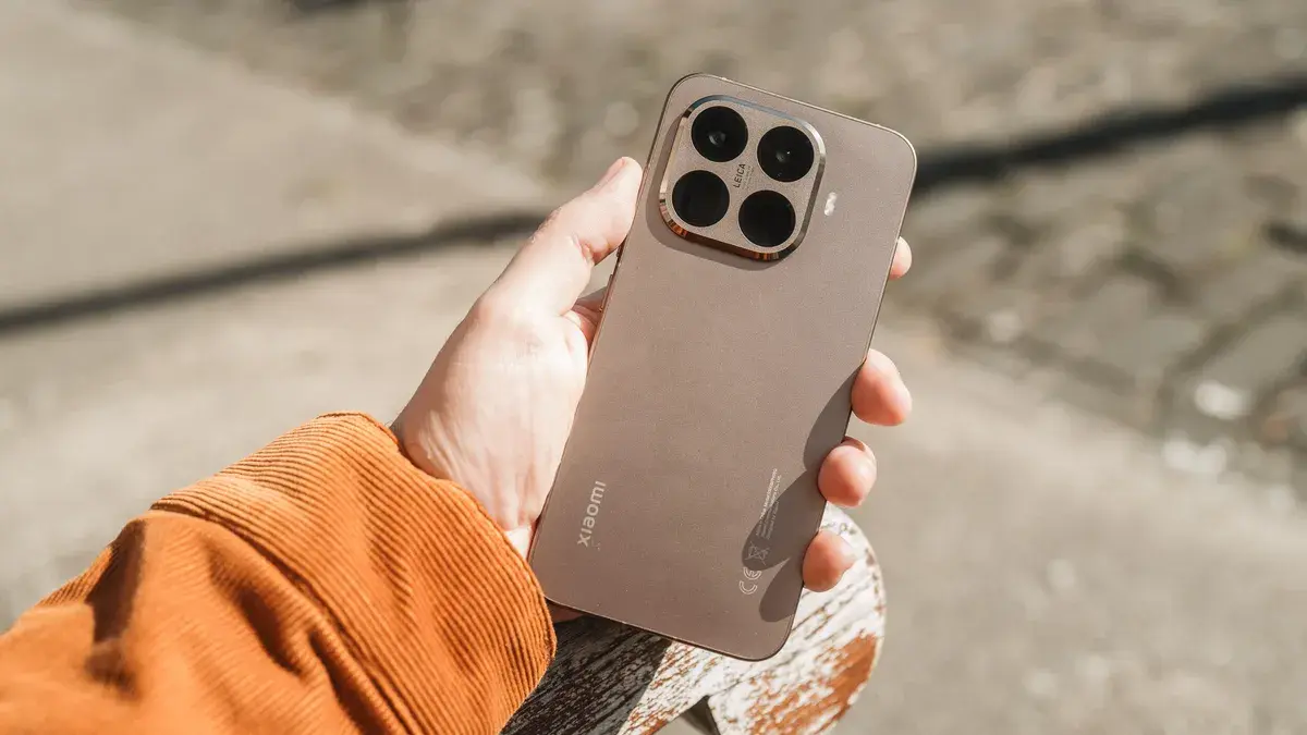 A brown Xiaomi 15T Pro smartphone held in one hand, showcasing the rear quad-camera module. This is one of the first devices to receive the HyperOS 3 Global update.